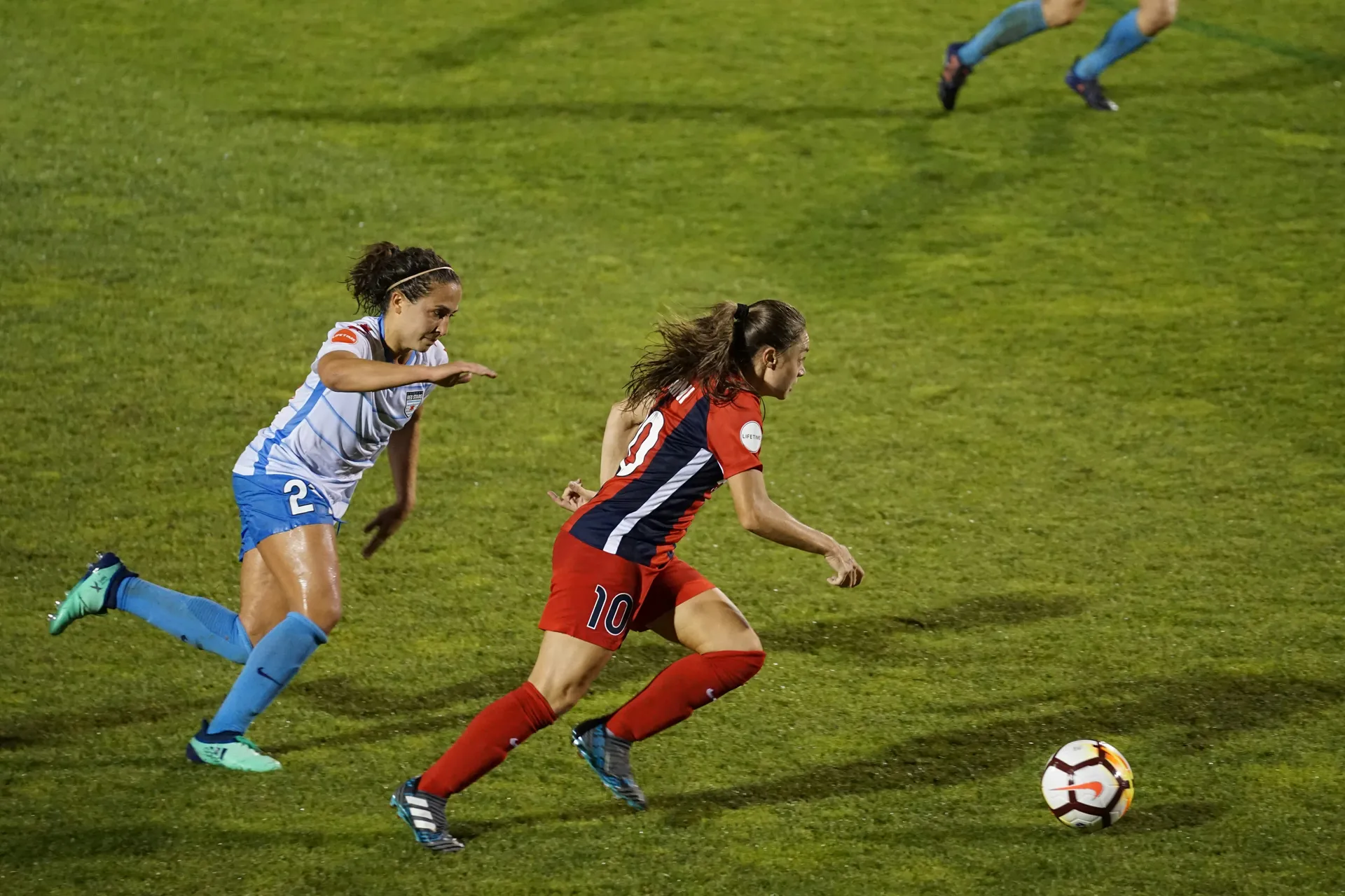 A number 10 breaking away with the ball under floodlights, chased by an opponent, several fixtures running at once