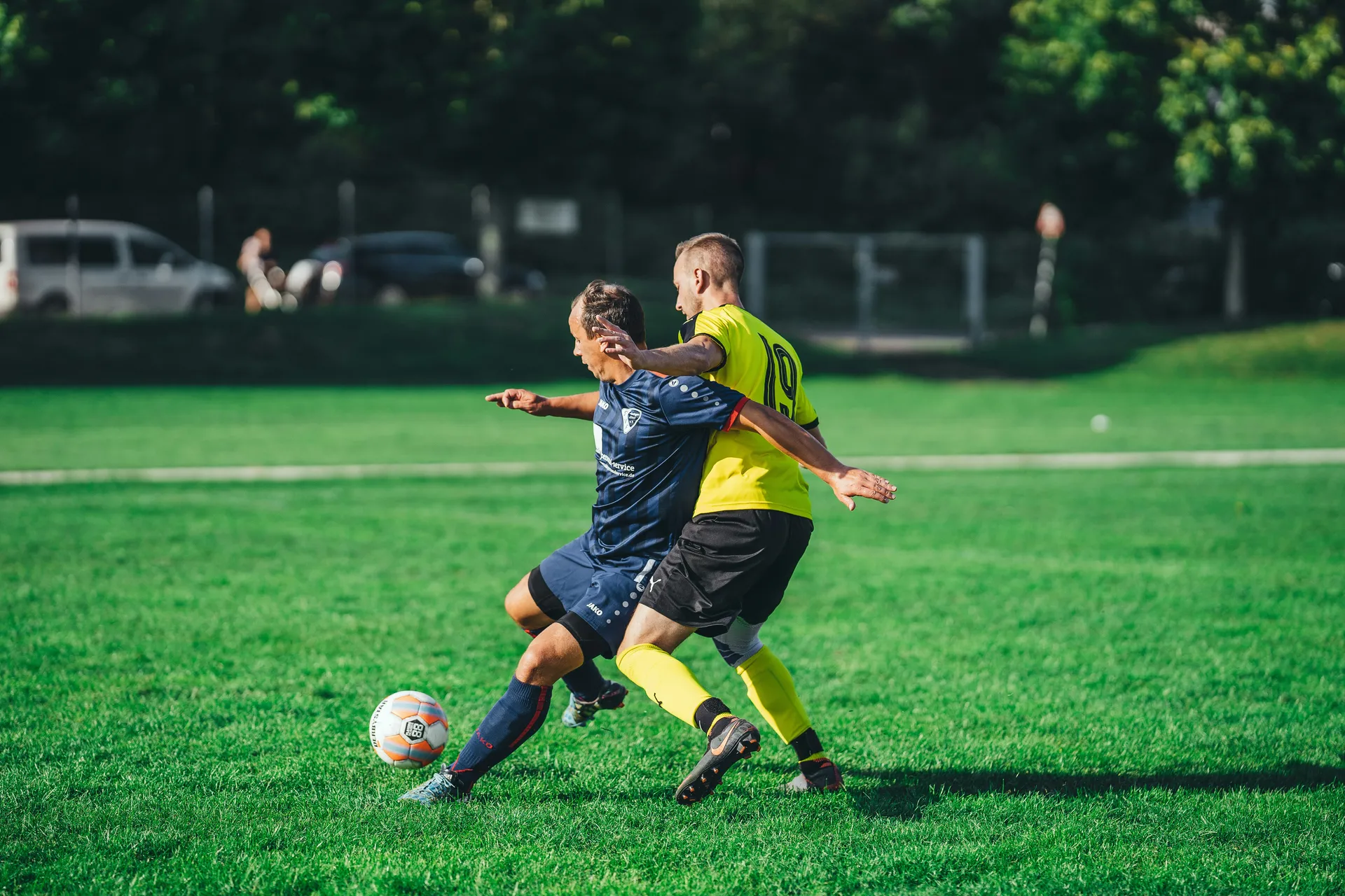 Two players from opposing teams battling for the ball on the pitch, like a head-to-head comparison of league management tools