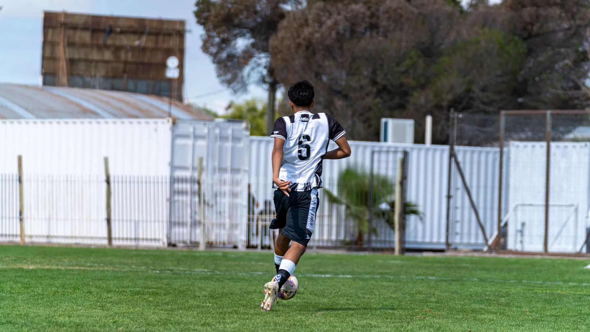 Jugador con el número 6 conduce el balón en una cancha municipal de pasto, el escenario habitual del fútbol 7 amateur