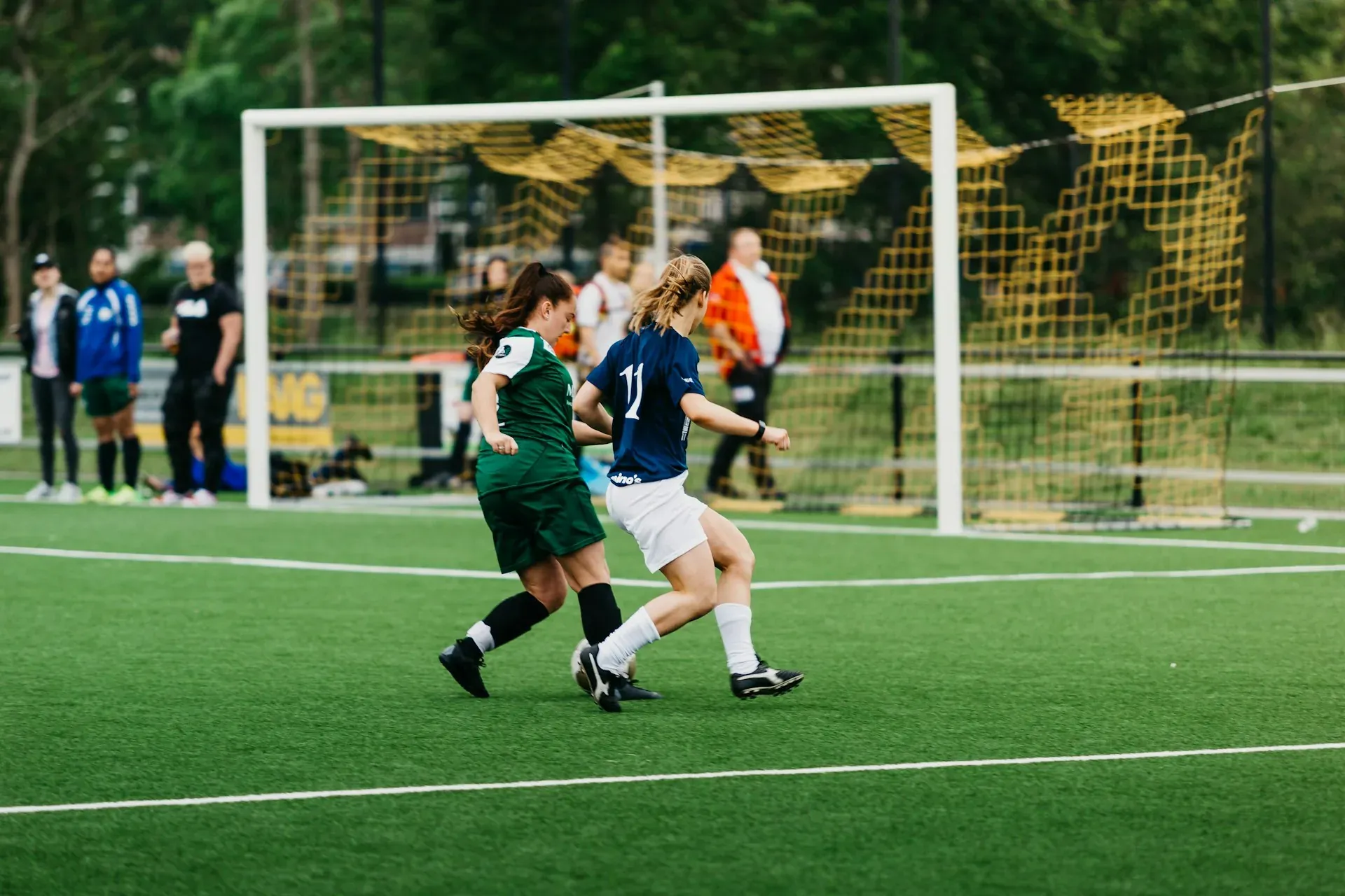 One-day football tournament: two players contest the ball on a 3G pitch, with spectators by the goal